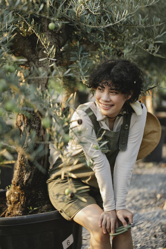 Young woman enjoys a sunny day in a lush, verdant garden with olive trees.